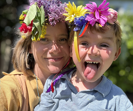 Caitlin and a child wearing flower crowns, smiling in a garden.