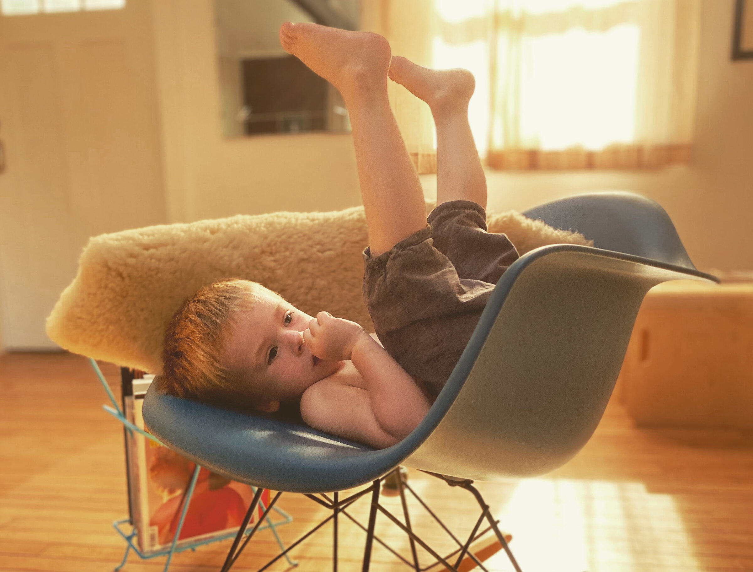 A child sitting upside down in a chair, in a cozy room.