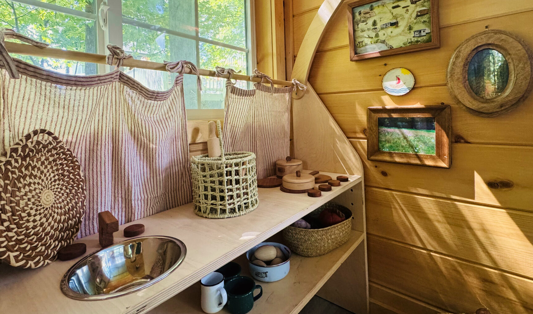 A cozy corner of the Nursery Cottage with wooden shelves of baskets, cups, and a small washbasin.