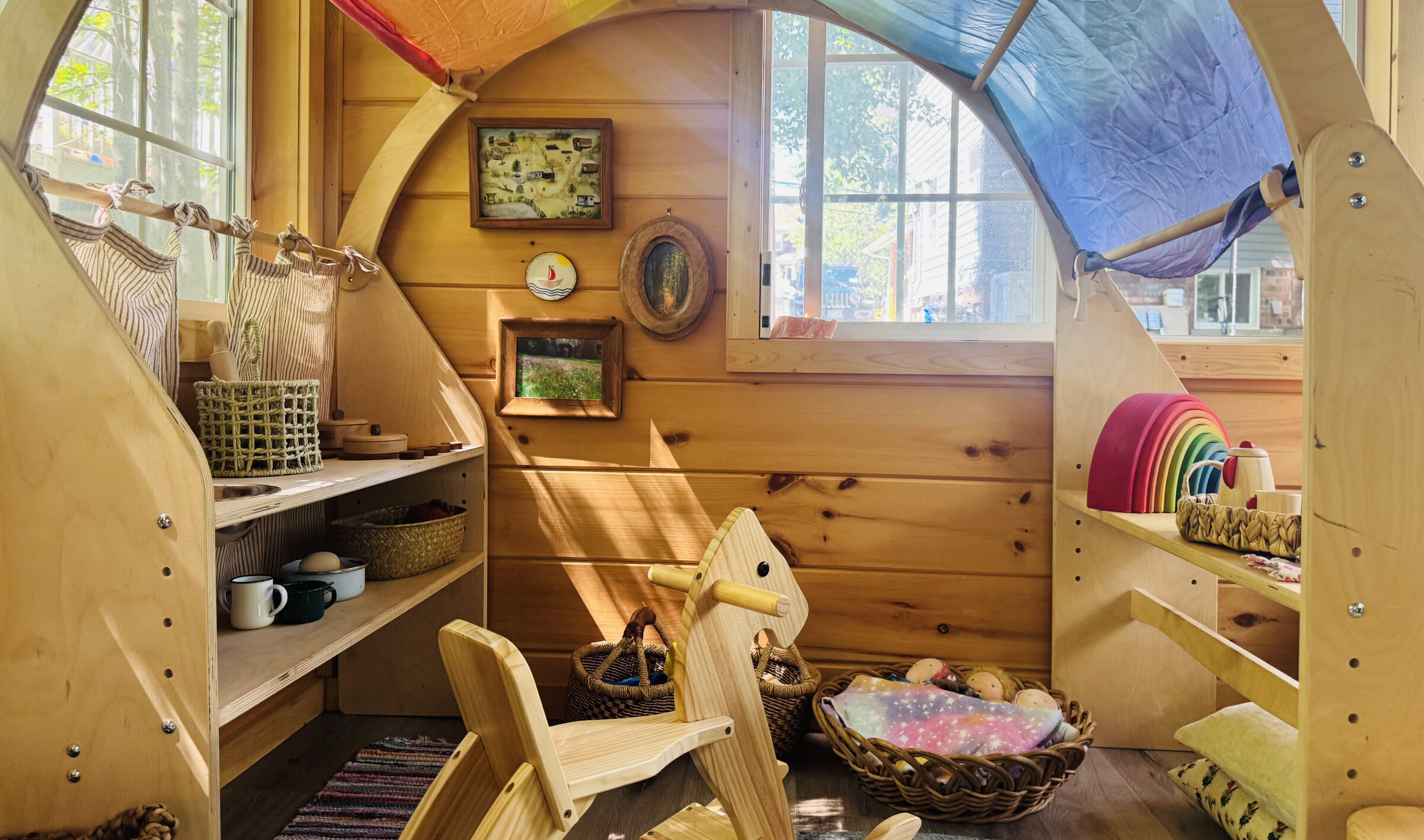 Inside the Nursery Cottage: warm wooden walls, simple natural toys, and soft light through round windows.